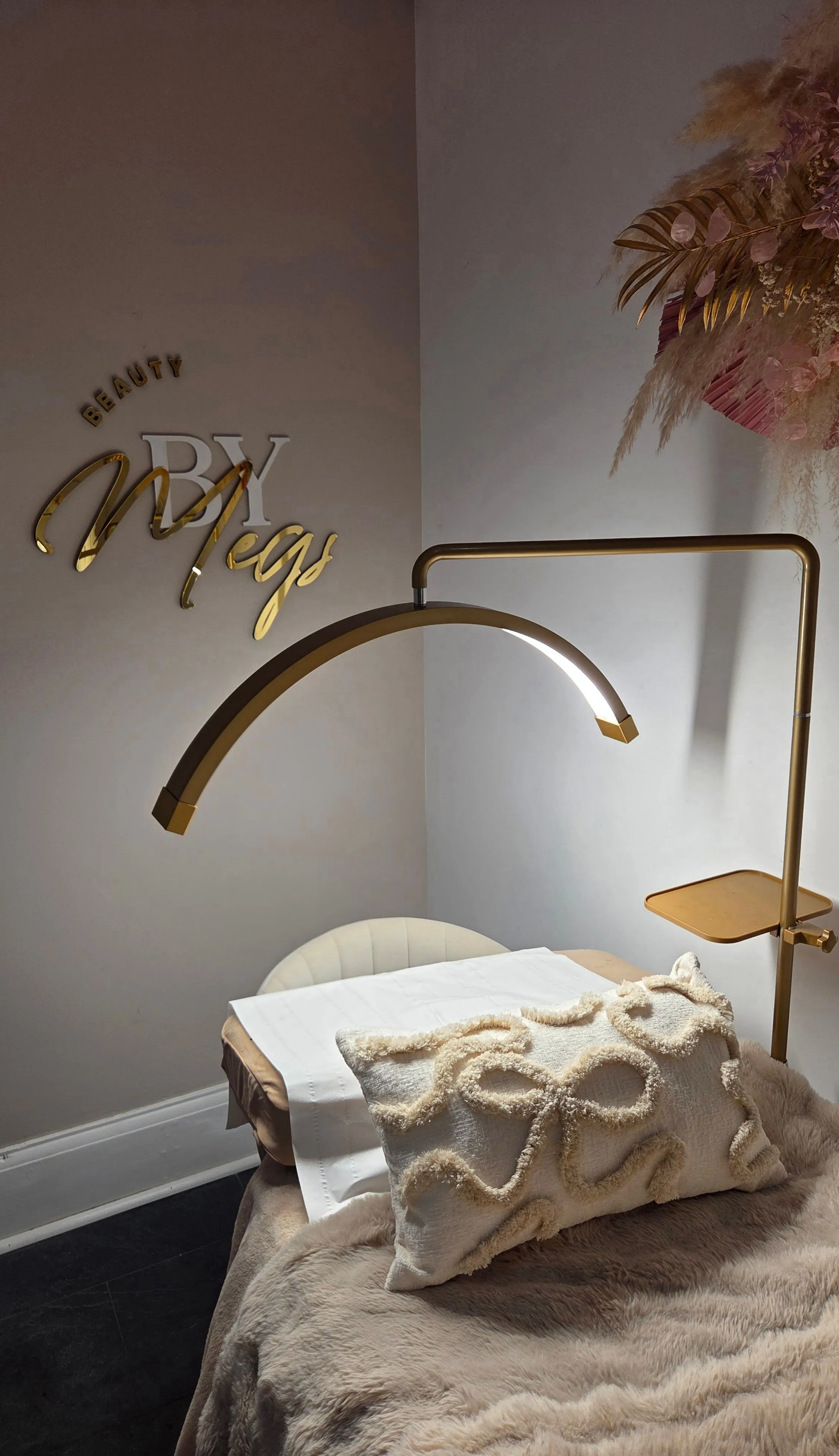 The Beauty By Megs studio: treatment bed, gold lamp and the gold script logo on the wall
